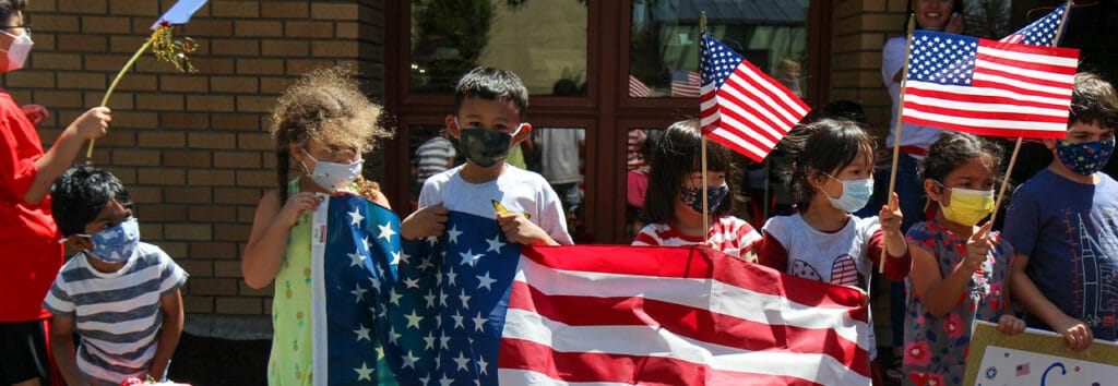 Early learning students with large and small USA flags, supporting the Olympics