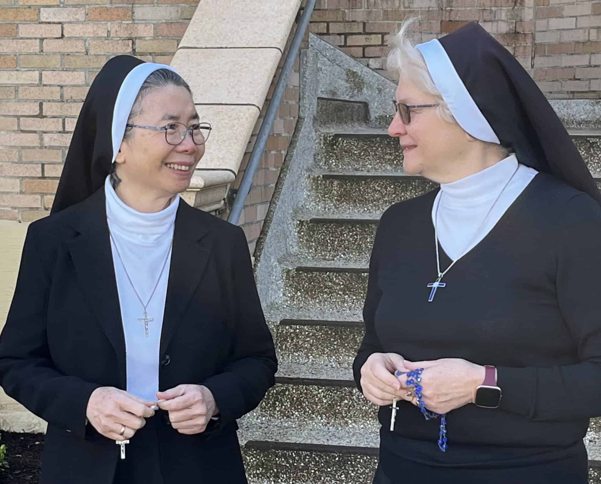 Sisters on front steps, rosaries in hands, smiling with each other