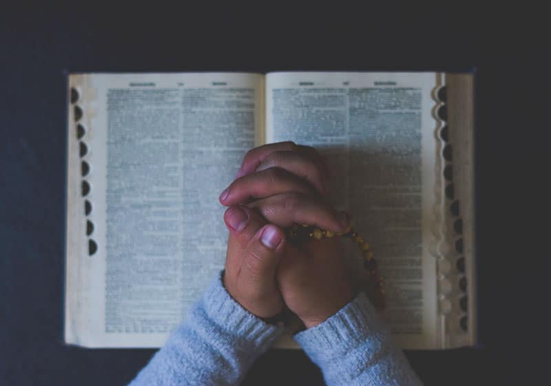 prayer hands with rosary on bible