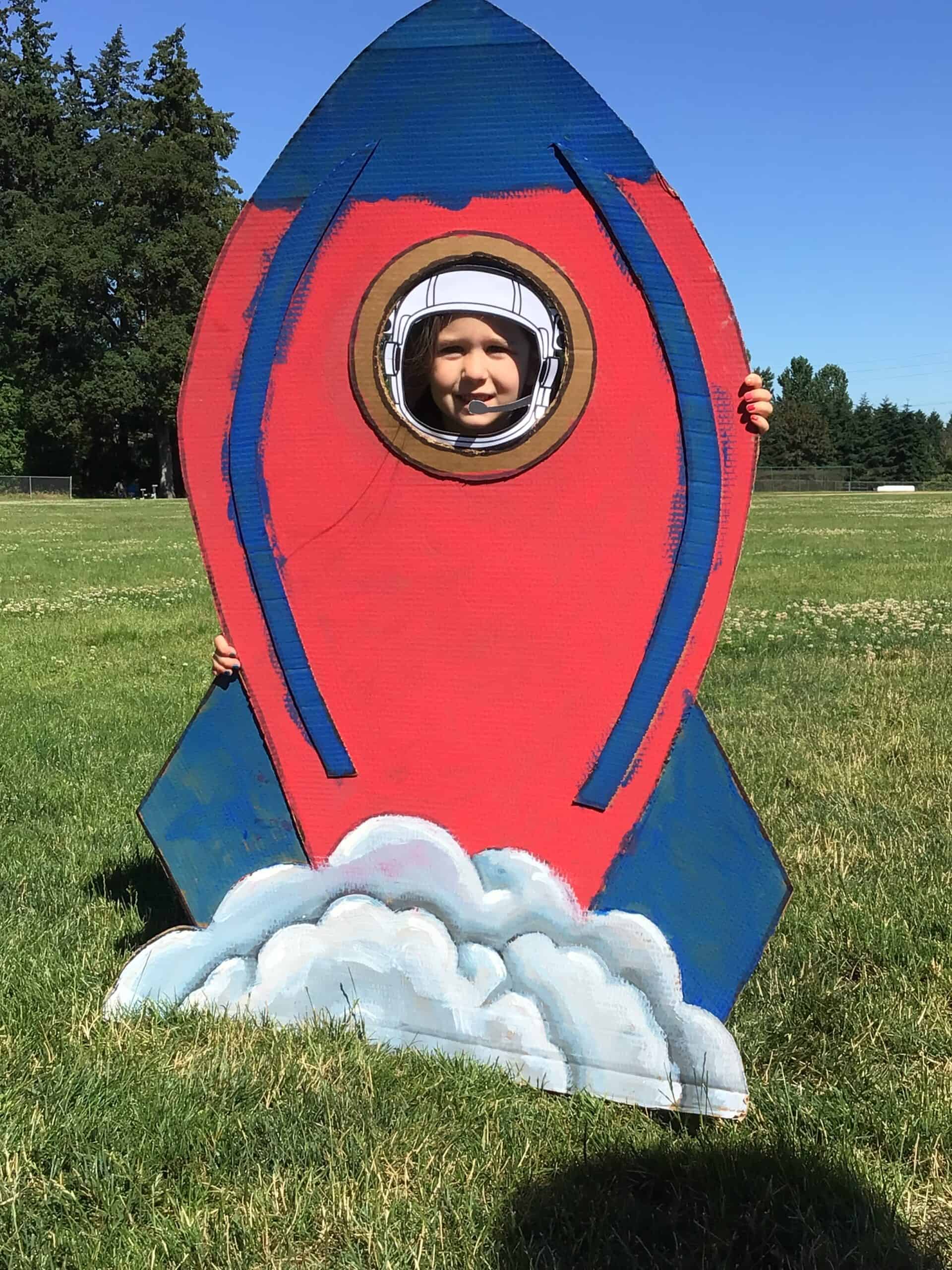 Summer Camp blast off; Student peeking their head through an opening of a cut out rocket ship.