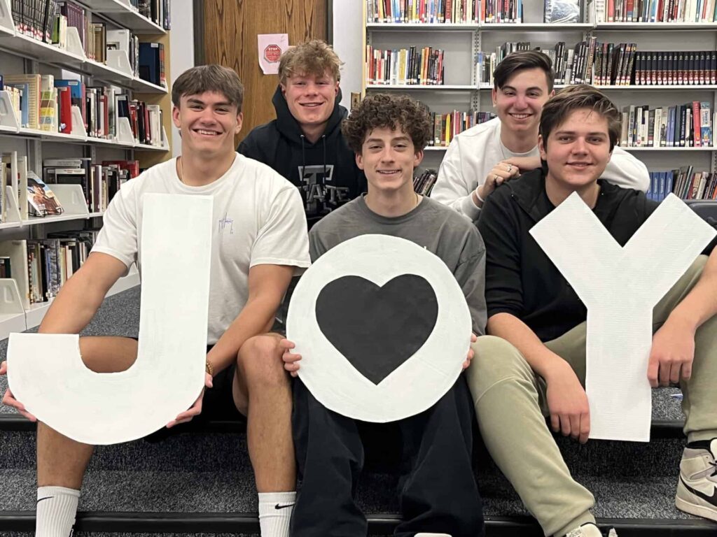 High school students holding cut out of J O Y