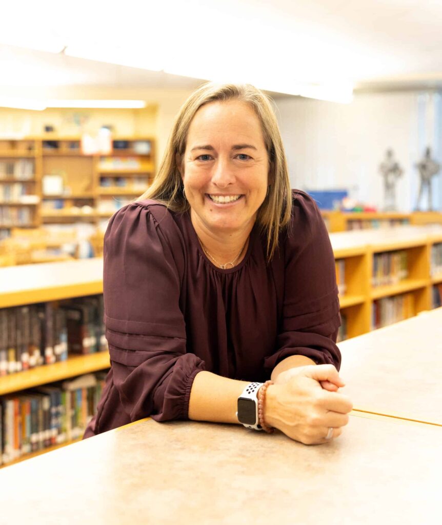 Dr. Sara Bruins, V C H S Principal, resting arms on a bookshelf