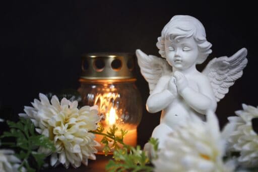 Angel,,votive,candle,and,flowers,on,black,background