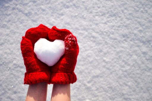 Female,hands,in,red,mittens,holding,snow,heart,on,snow