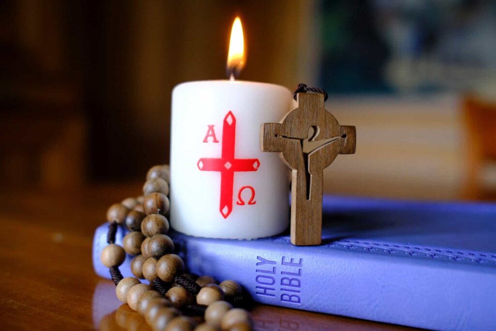 Bible with wooden rosary and alpha omega lit candle
