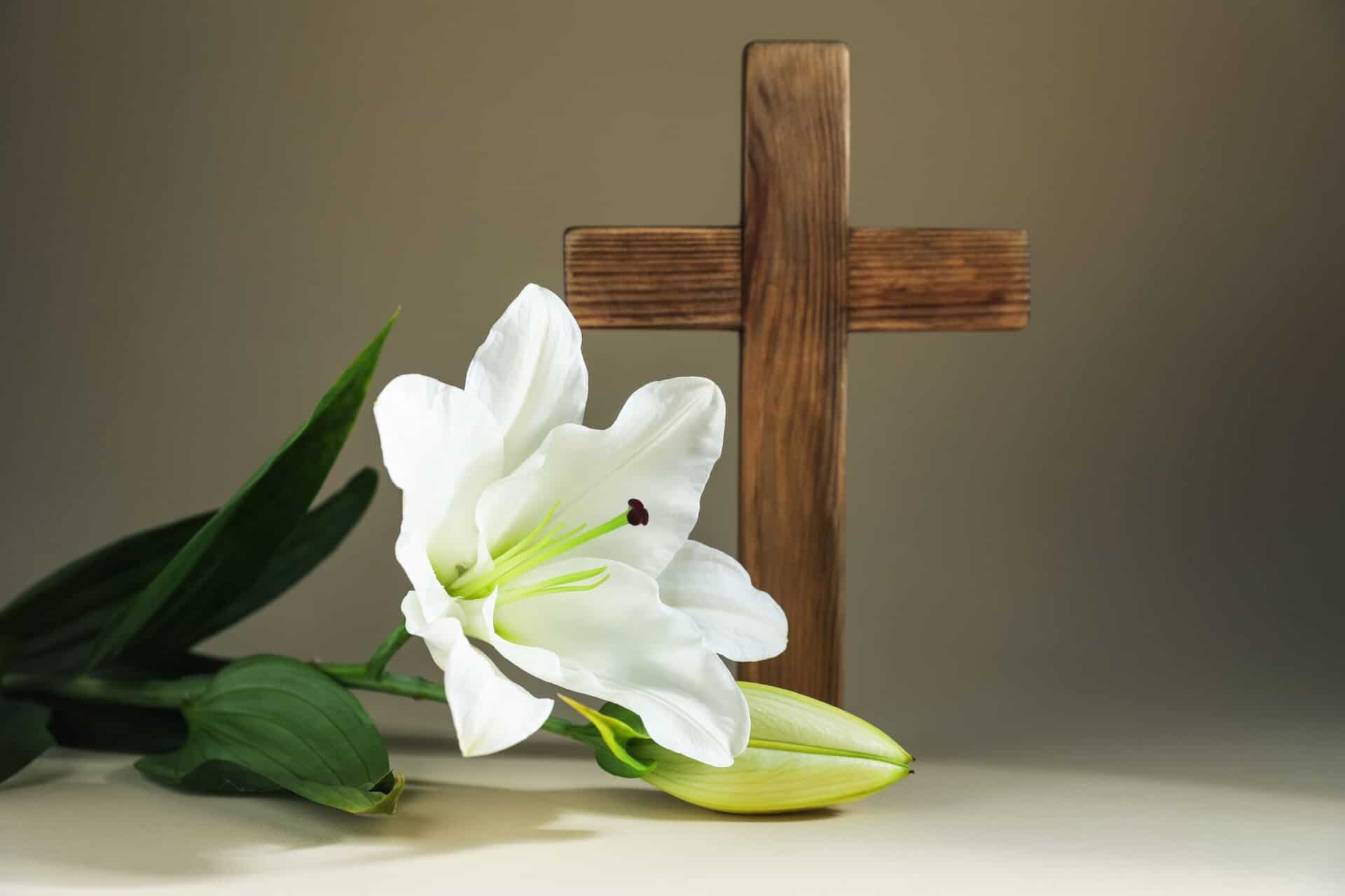 Wooden cross with an Easter Lily laying in front of it.