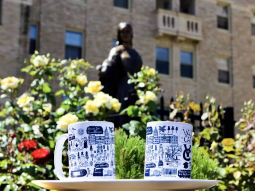 Two white and blue Valley Catholic mugs pictured in front of the statue of Mary